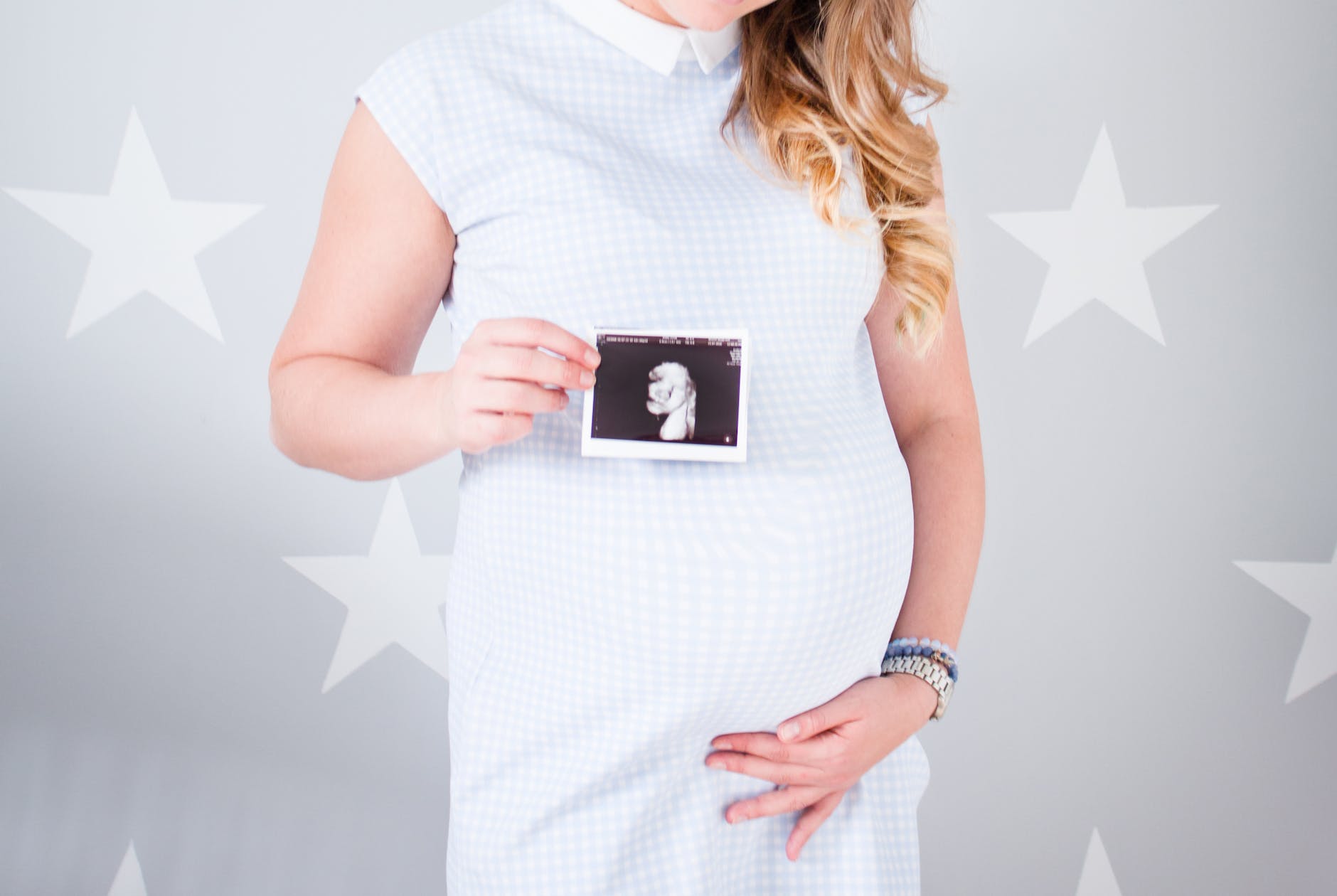 woman wearing white cap sleeved dress holding ultrasound result photo