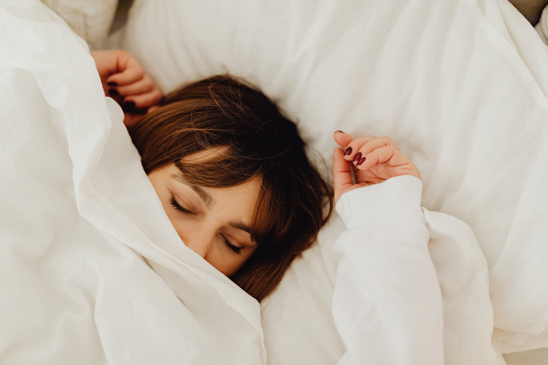 woman lying on bed covering her face with a white blanket